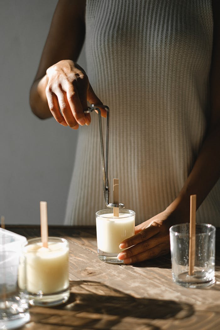 our-story Unrecognizable African American female standing at wooden table with candle and steel wick dipper in light room with sunlight