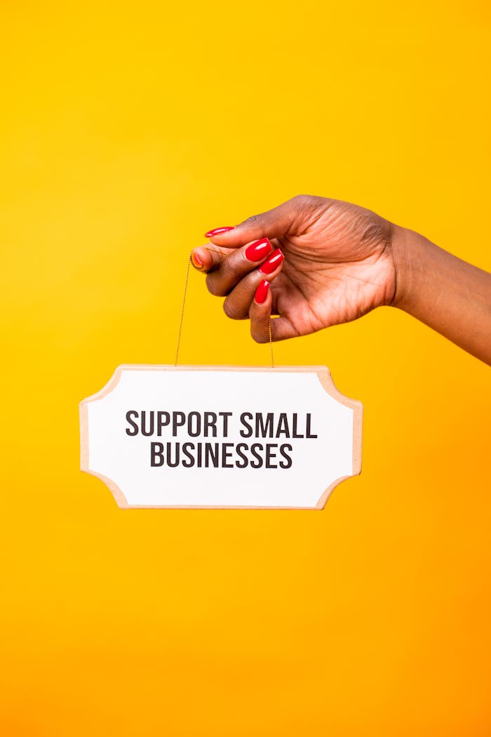 gallery-04 A hand holding a 'Support Small Businesses' sign on a vibrant yellow background.